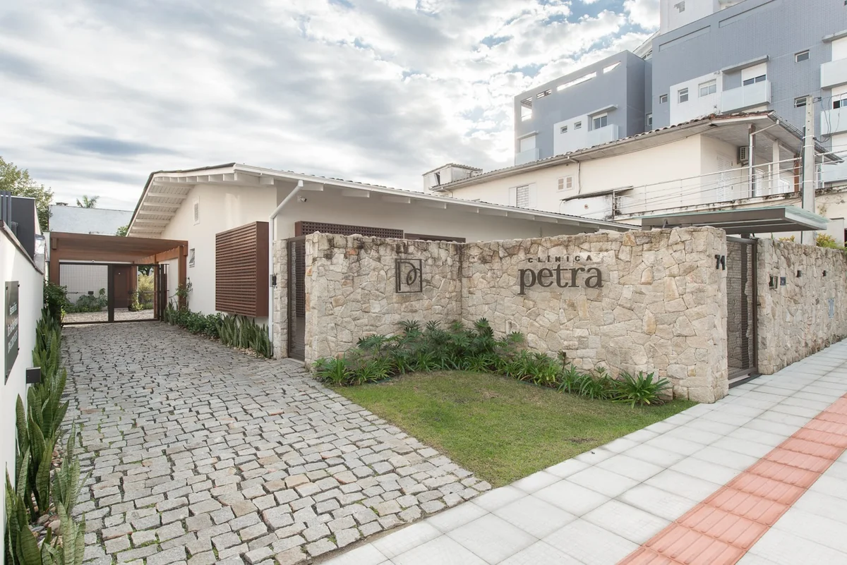 Fachada da Clínica Petra, em Criciúma/SC: muro de pedra com a marca da clínica e entrada em paralelepípedo